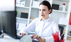 Woman holding pen in her mouth while using computer