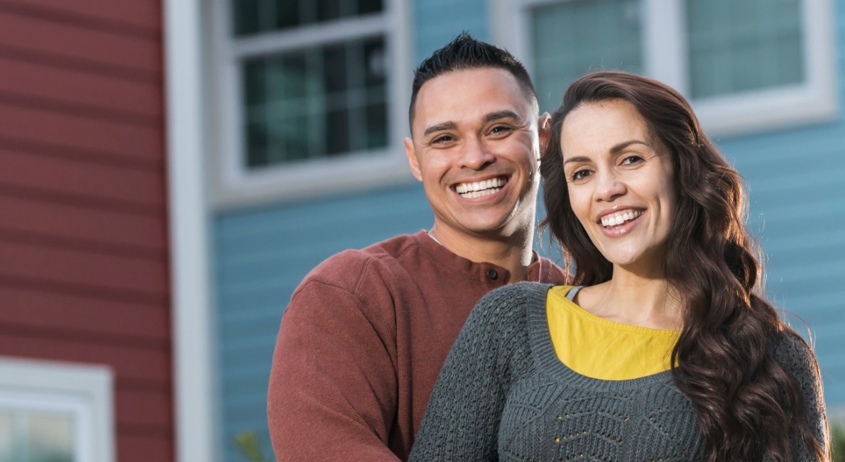 Young couple smiling in front of house