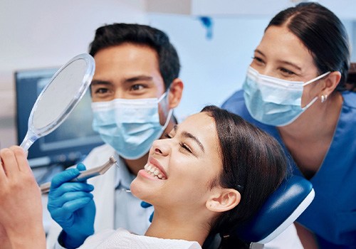 Patient smiling at reflection with dental hygienist and dentist