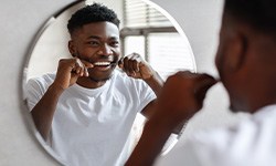 Man smiling while flossing in bathroom