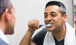 Man with towel around neck brushing teeth in mirror