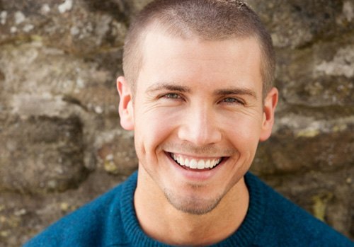 Man in blue shirt smiling in front of brick wall