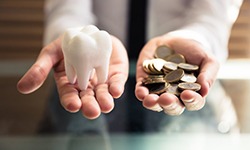 cost of dental implants in San Antonio represented by hands holding coins and tooth