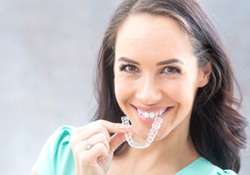 A young woman wearing a teal blouse and preparing to insert her Invisalign aligner into her mouth