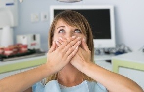 Woman in need of sedation dentistry covering her mouth in dental chair