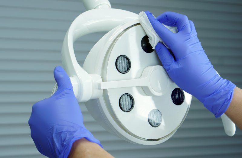 a dental staff member wearing gloves and cleaning the overhead light used during an appointment