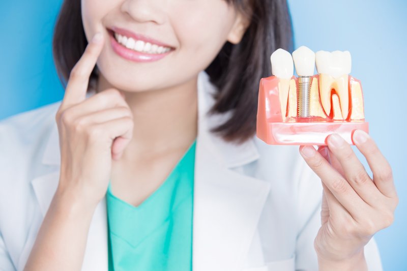 Female dentist holding implant model and pointing to tooth
