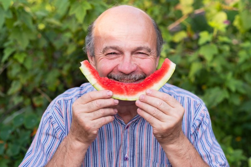 senior smiling and eating watermelon with dental implants