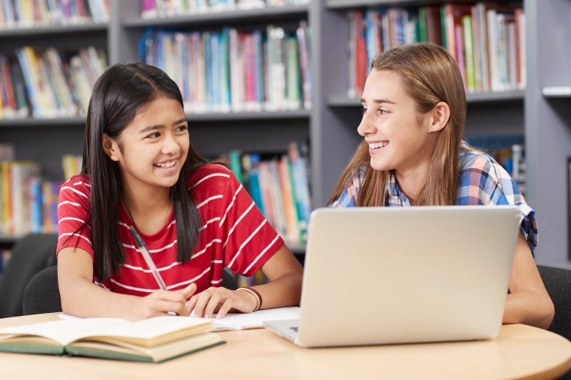 two high school students laughing in library