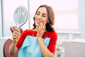 Woman looking at smile in mirror after getting dental implants