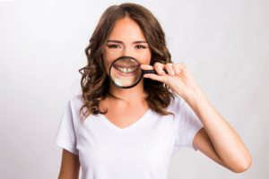 Woman in white t-shirt in front of white background holding magnifying glass up to her diastema