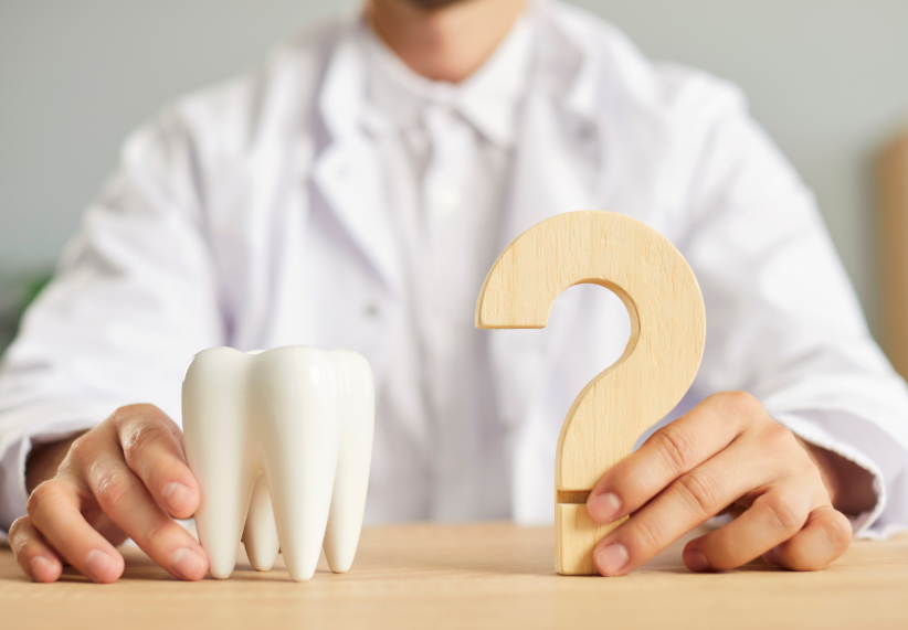 Dentist holding model tooth in one hand and a wooden question mark in the other